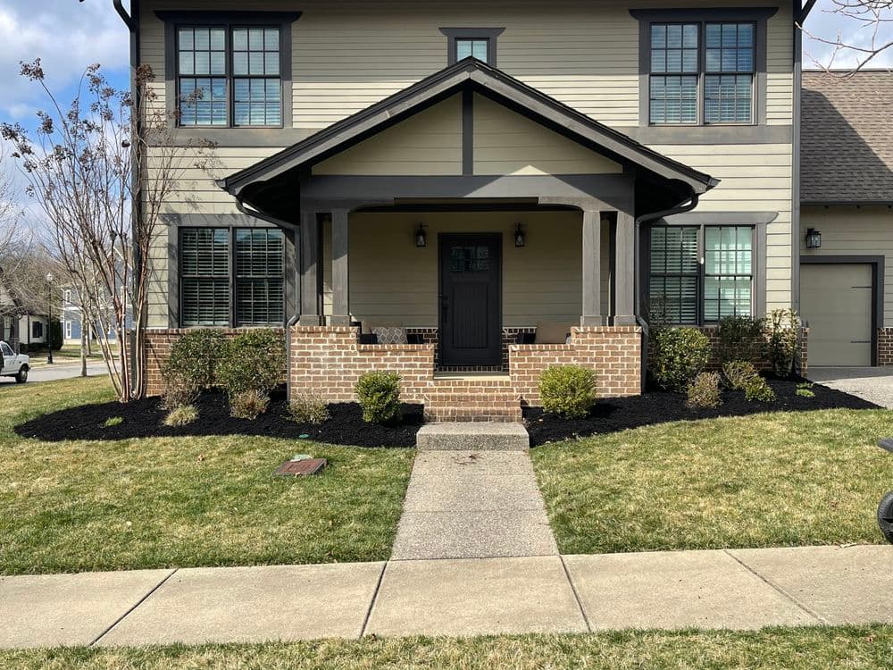Front view of a modern two-story home with a porch, lush landscaping, and a concrete walkway.