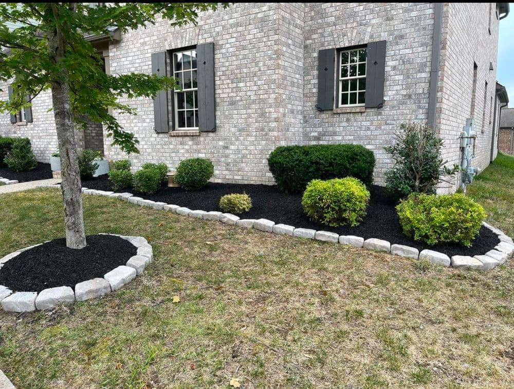 Brick home with landscaped yard featuring shrubs, mulch, and stone border along foundation.